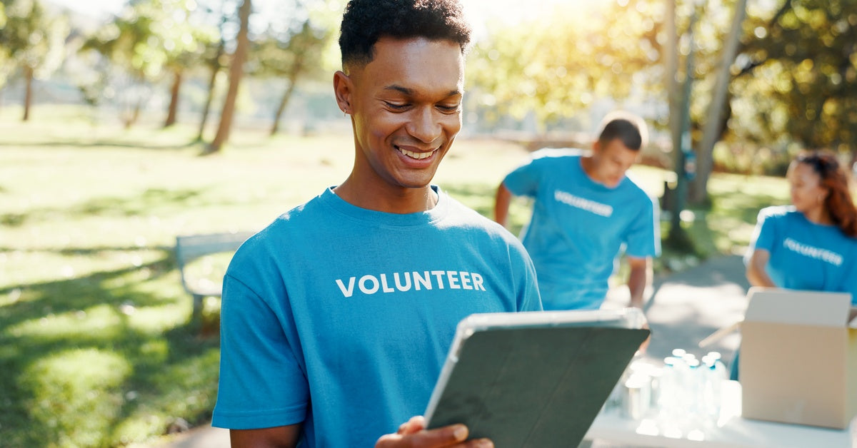 A smiling volunteer in a blue T-shirt checking notes in a large folder at an outdoor donation drive.