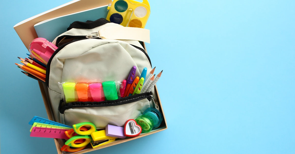 A top view of a box filled with a backpack and school supplies, such as sharpeners, notebooks, and colored pencils.