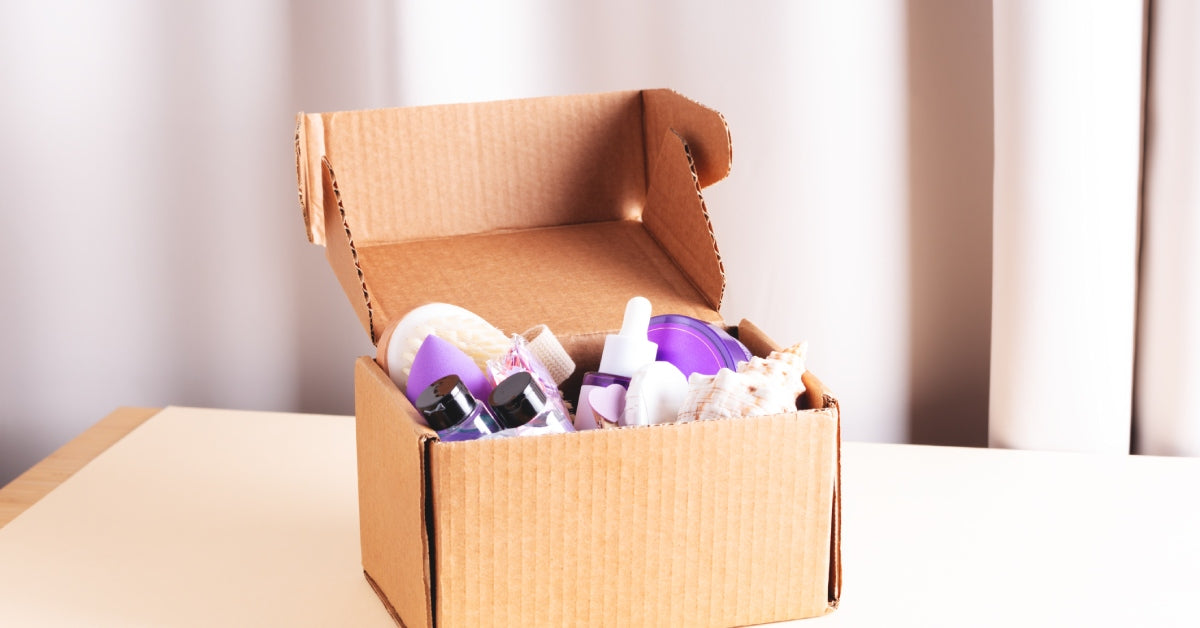 A cardboard box containing a variety of body care and skin care products sitting on a table with a white curtain behind it.