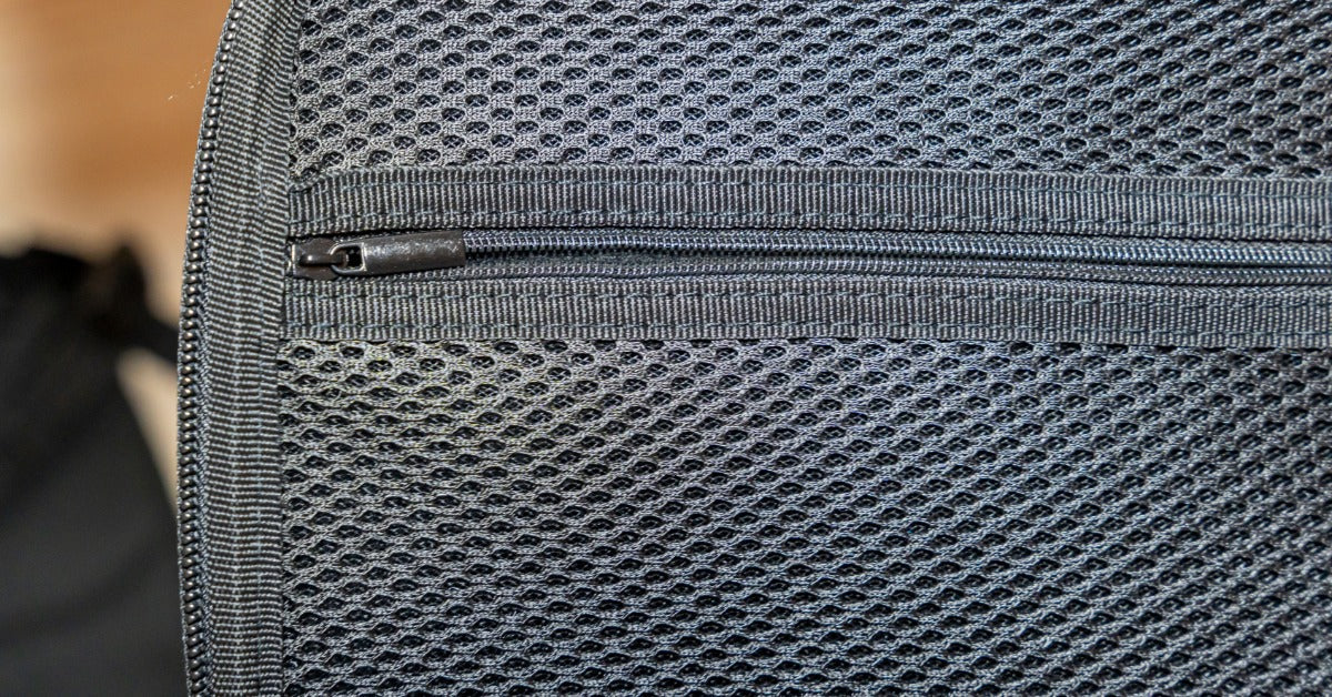 An extreme close-up of the edge of a black textured mesh pocket with a small zipper securing its opening.