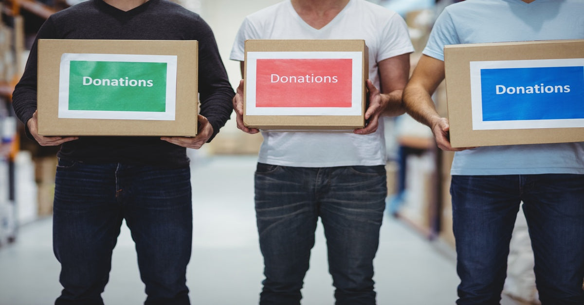 Three people stand in a line, holding cardboard boxes up with "donations" signs displayed on the front.