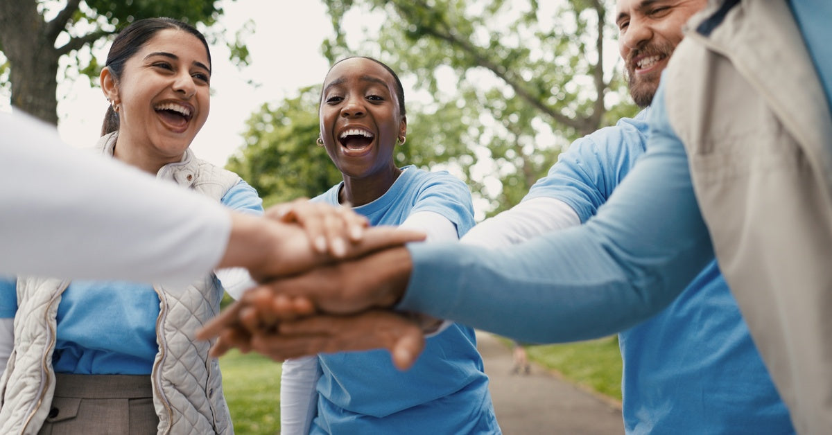 A diverse group of individuals wearing matching blue shirts stand outdoors, joining hands in a show of unity.