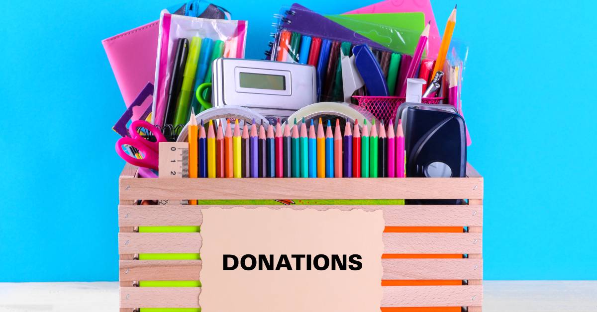 A wooden box labeled "Donations" contains an array of school supplies, including colored pencils, a calculator, and markers.