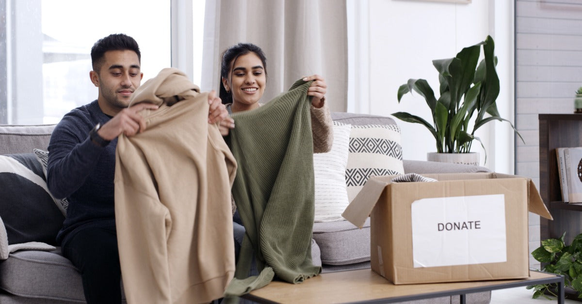 A man and a woman are on a couch with a small table beside them and a box with a "Donate" sign on its side.