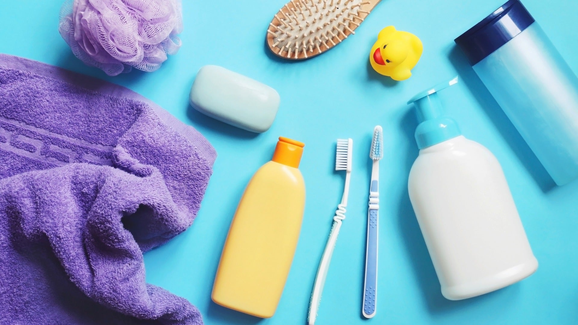 Several personal care products, including a purple towel, toothbrushes, and lotion, are spread out on a blue surface.