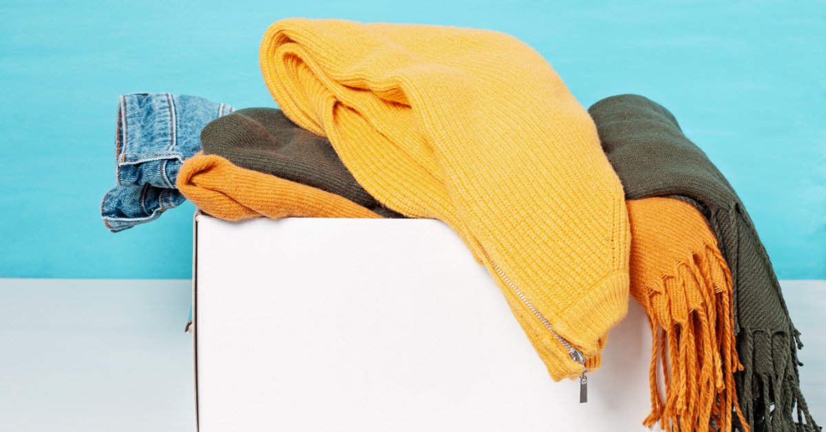 A close-up of a white cardboard box filled with winter clothing items, including scarves and a denim jacket.