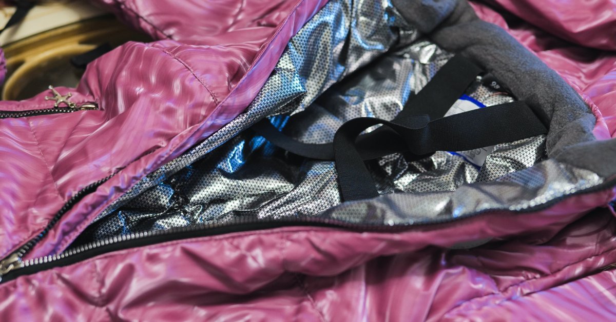 A close-up of a magenta winter jacket with a silver lining and black zippers in a well-lit environment.